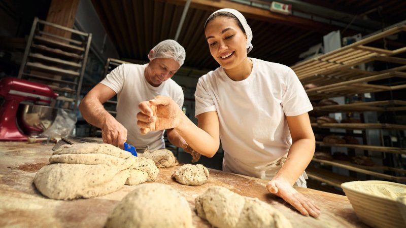 Ein Bäcker und eine Bäckerin beim Teig kneten